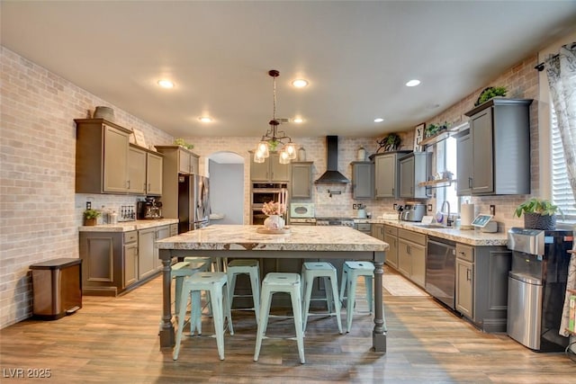 kitchen featuring wall chimney range hood, a breakfast bar area, appliances with stainless steel finishes, a kitchen island, and decorative light fixtures