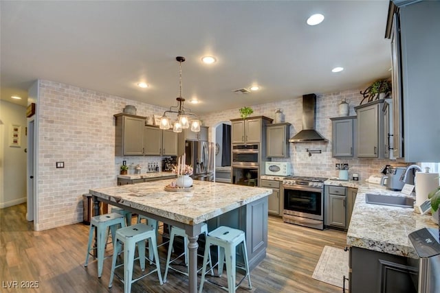 kitchen featuring a kitchen bar, a center island, stainless steel appliances, light stone countertops, and wall chimney exhaust hood