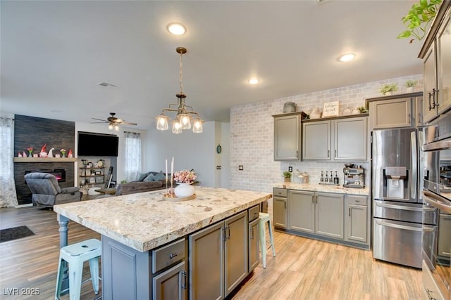 kitchen with backsplash, stainless steel refrigerator with ice dispenser, a kitchen breakfast bar, and light wood finished floors