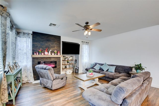 living room with a ceiling fan, visible vents, a fireplace, and wood finished floors