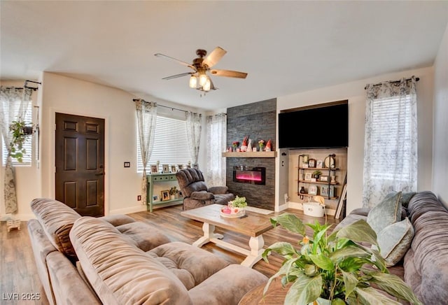 living area with a stone fireplace, wood finished floors, a ceiling fan, and baseboards