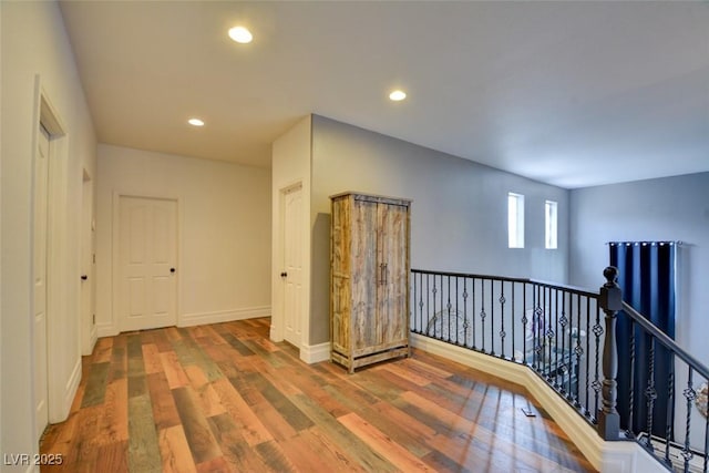 corridor featuring an upstairs landing, baseboards, wood finished floors, and recessed lighting