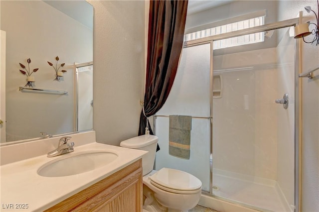 bathroom featuring a shower with door, vanity, and toilet