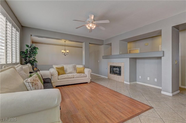 living room featuring light tile patterned flooring, ceiling fan with notable chandelier, and a tile fireplace