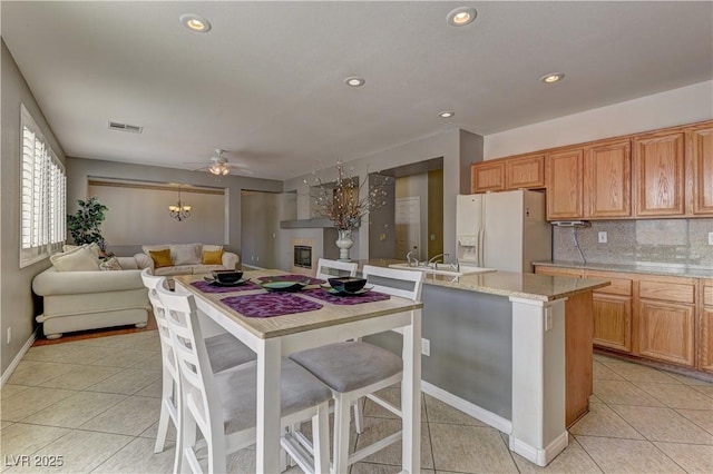 kitchen featuring light tile patterned flooring, a breakfast bar area, decorative backsplash, white fridge with ice dispenser, and light stone counters