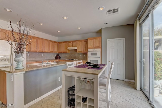 kitchen with light tile patterned floors, gas cooktop, double oven, a center island, and tasteful backsplash