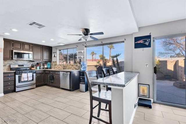 kitchen featuring decorative backsplash, dark brown cabinets, stainless steel appliances, and a kitchen breakfast bar