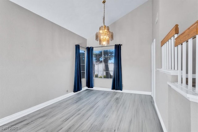 unfurnished dining area featuring an inviting chandelier, high vaulted ceiling, and light hardwood / wood-style floors