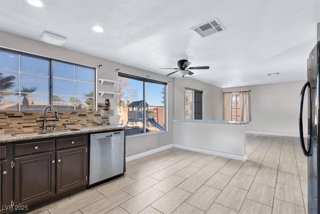 kitchen with sink, black fridge, stainless steel dishwasher, dark brown cabinetry, and light stone countertops