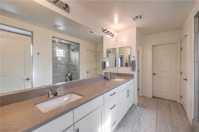 bathroom featuring double vanity, visible vents, a stall shower, and a sink