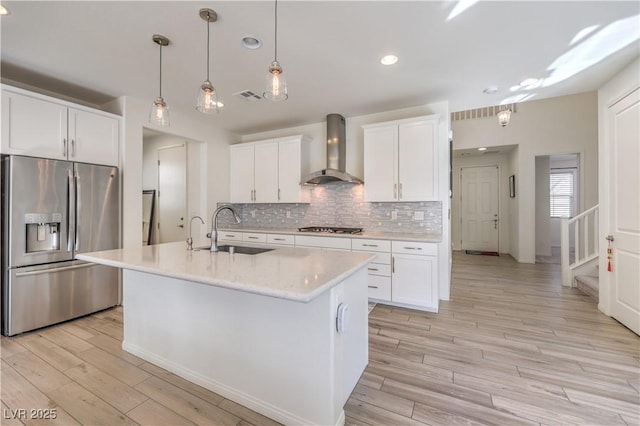 kitchen featuring wall chimney exhaust hood, sink, stainless steel appliances, a kitchen island with sink, and white cabinets