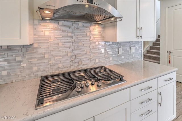 kitchen with backsplash, range hood, white cabinetry, stainless steel gas stovetop, and light stone countertops