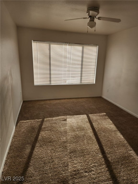 empty room with ceiling fan and dark colored carpet