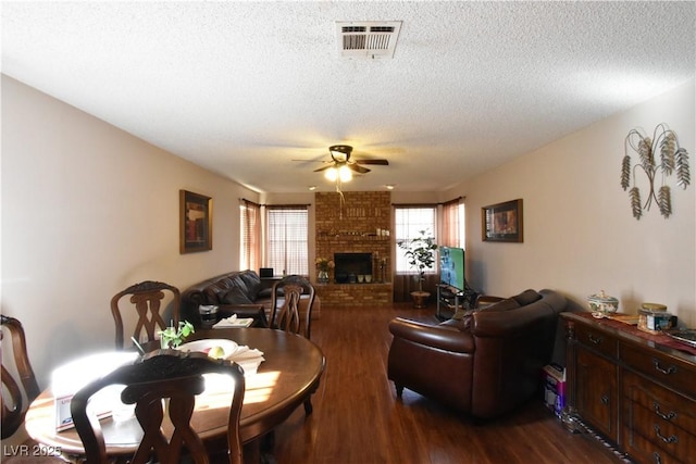 dining space featuring a brick fireplace, dark hardwood / wood-style floors, a textured ceiling, and ceiling fan