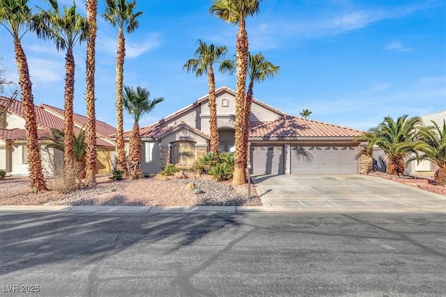 mediterranean / spanish home with concrete driveway, an attached garage, a tiled roof, and stucco siding