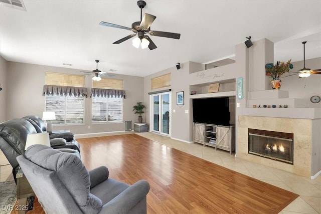 living room featuring a tile fireplace, ceiling fan, and light wood-type flooring