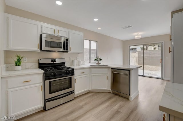 kitchen with sink, light wood-type flooring, white cabinetry, stainless steel appliances, and light stone countertops