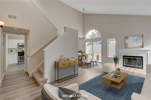 living room with a fireplace, high vaulted ceiling, light hardwood / wood-style floors, and an inviting chandelier