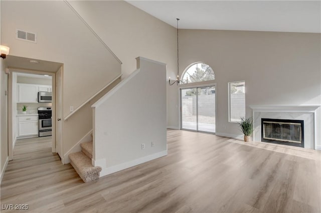 unfurnished living room with light hardwood / wood-style floors, high vaulted ceiling, a chandelier, and a fireplace