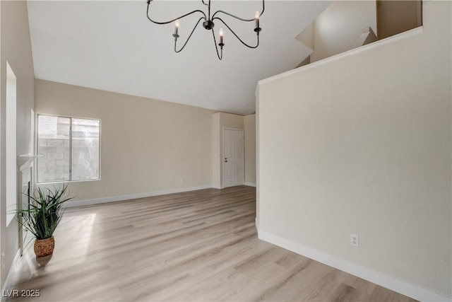 spare room featuring a notable chandelier, light wood-type flooring, and vaulted ceiling