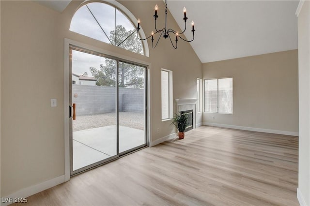 unfurnished living room with high vaulted ceiling, a notable chandelier, and light hardwood / wood-style floors