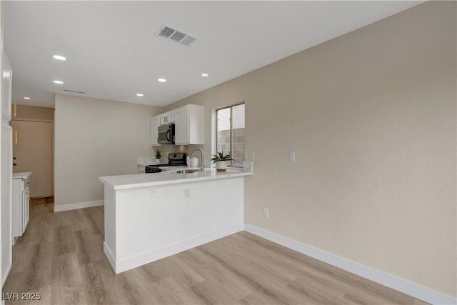 kitchen with white cabinetry, kitchen peninsula, appliances with stainless steel finishes, and light hardwood / wood-style flooring