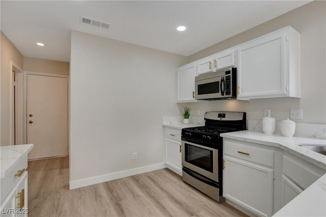 kitchen featuring sink, light stone counters, light wood-type flooring, white cabinetry, and stainless steel appliances