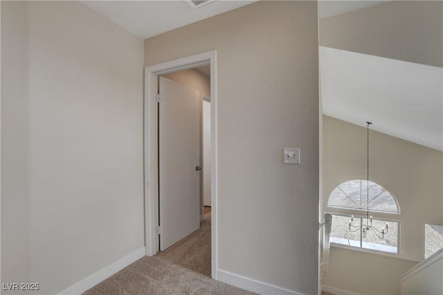 hallway featuring light carpet, lofted ceiling, and a chandelier