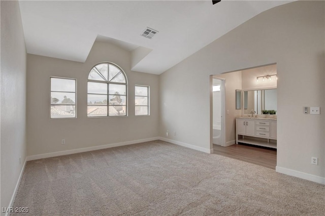 unfurnished bedroom with vaulted ceiling, connected bathroom, light colored carpet, and sink