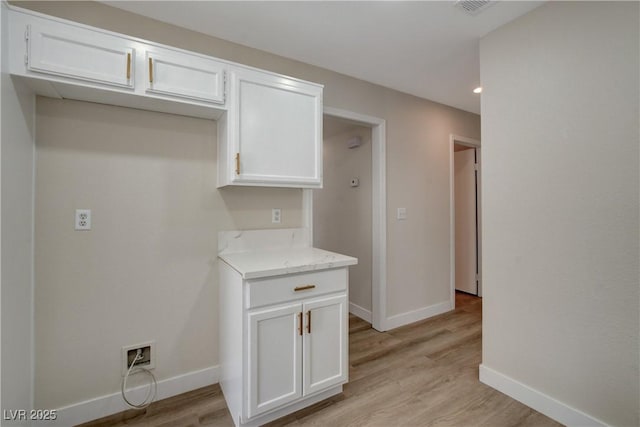 kitchen featuring white cabinets, light wood-type flooring, and light stone counters