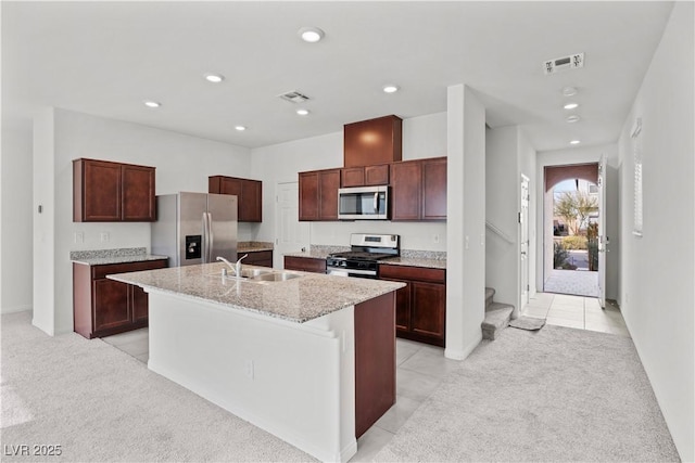 kitchen with sink, stainless steel appliances, light stone counters, an island with sink, and light carpet