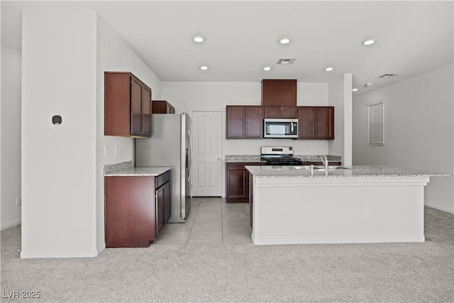 kitchen with stainless steel appliances, a kitchen island with sink, light colored carpet, and light stone counters