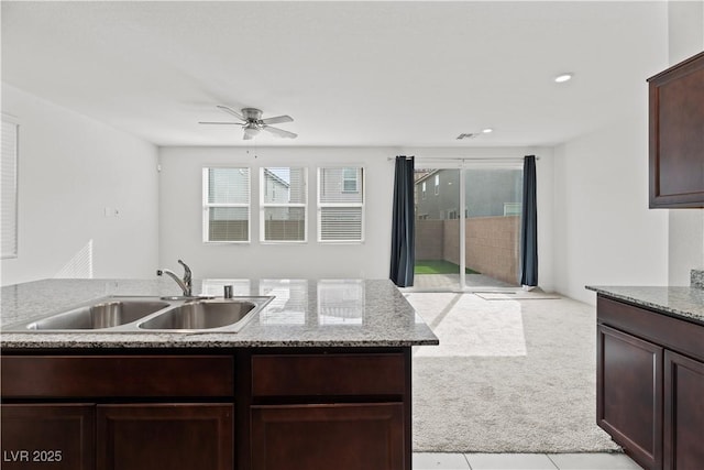 kitchen with sink, ceiling fan, light stone counters, dark brown cabinetry, and light carpet