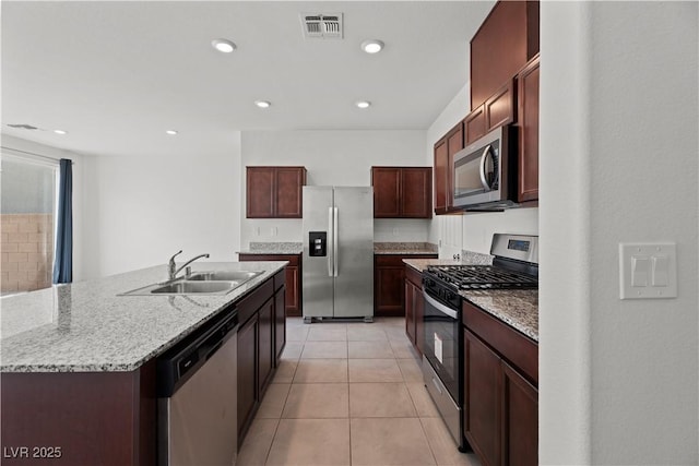 kitchen featuring sink, light tile patterned floors, stainless steel appliances, light stone countertops, and an island with sink