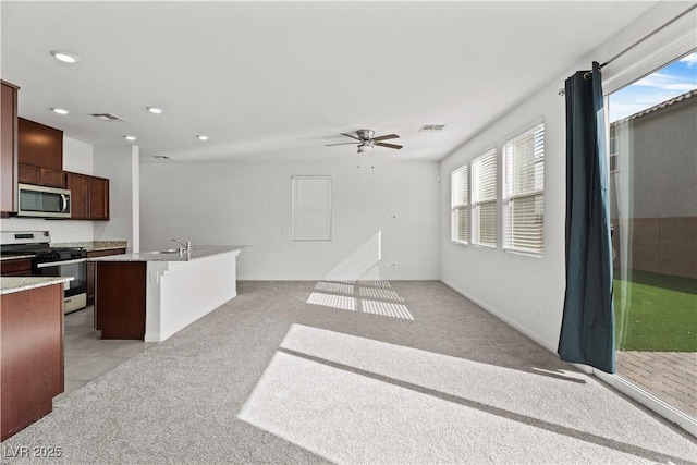 kitchen with a breakfast bar, light colored carpet, appliances with stainless steel finishes, an island with sink, and ceiling fan