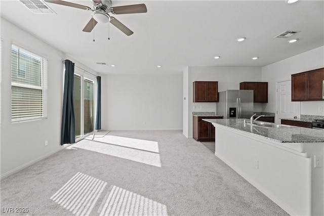 kitchen featuring sink, light stone counters, stainless steel fridge with ice dispenser, a center island with sink, and light carpet