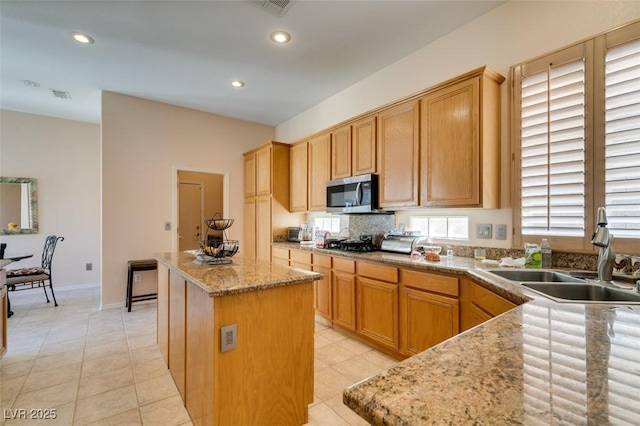 kitchen with light tile patterned flooring, a center island, sink, and light stone counters