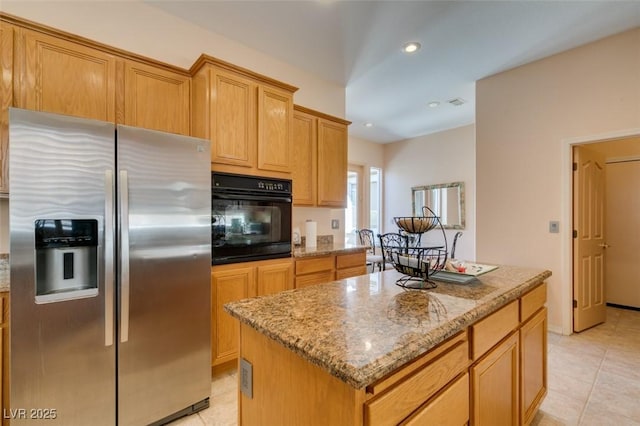 kitchen with a kitchen island, black oven, stainless steel fridge, light tile patterned floors, and light stone countertops