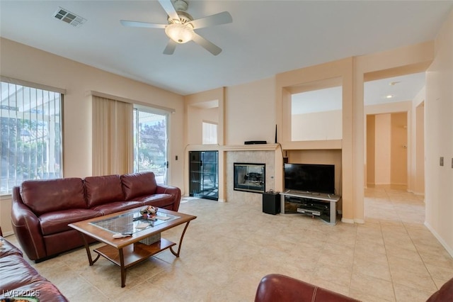 living room featuring a tiled fireplace, light tile patterned floors, and ceiling fan