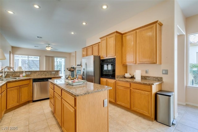 kitchen with a kitchen island, appliances with stainless steel finishes, sink, light tile patterned floors, and light stone counters