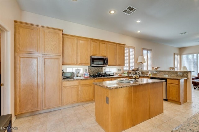 kitchen with light stone counters, a center island, kitchen peninsula, and appliances with stainless steel finishes