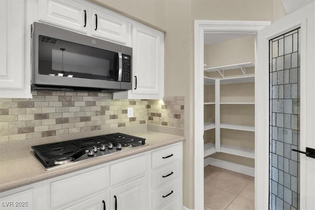 kitchen with appliances with stainless steel finishes, light tile patterned floors, white cabinets, and decorative backsplash