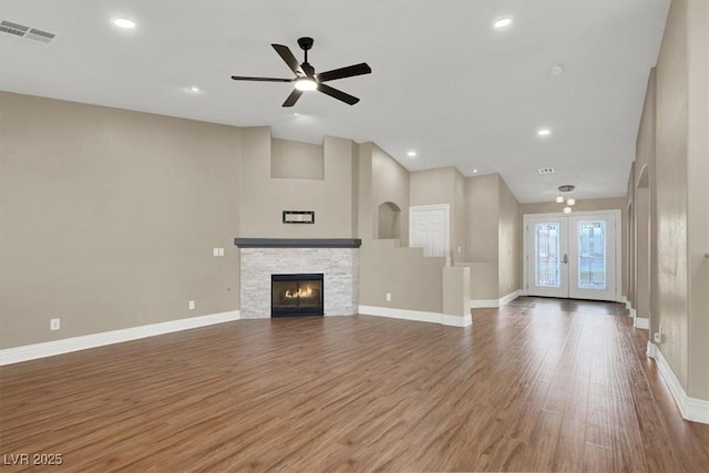 unfurnished living room featuring wood-type flooring, ceiling fan, a fireplace, and french doors