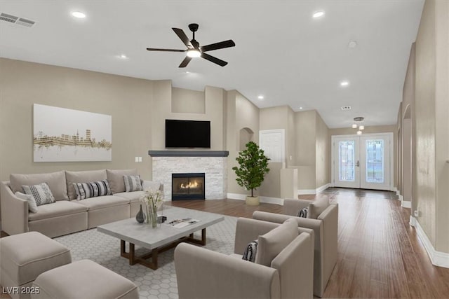 living room with french doors, ceiling fan, a stone fireplace, and light wood-type flooring