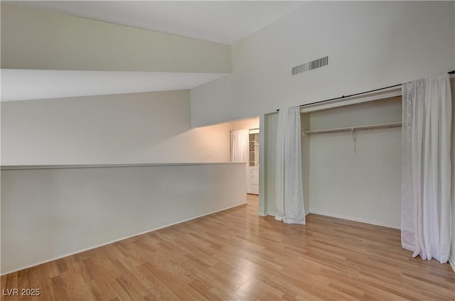 unfurnished bedroom featuring lofted ceiling, light hardwood / wood-style floors, and a closet