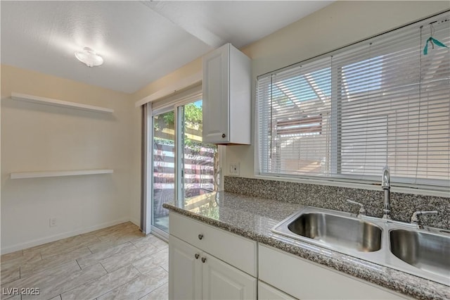 kitchen with white cabinetry, stone countertops, and sink