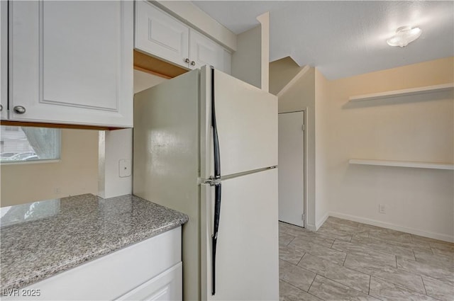 kitchen featuring white cabinetry, light stone countertops, and white fridge