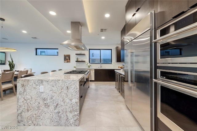 kitchen featuring sink, light stone counters, island range hood, a center island, and appliances with stainless steel finishes