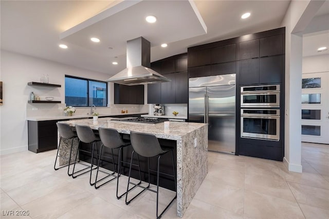 kitchen featuring a breakfast bar area, appliances with stainless steel finishes, a center island, light stone counters, and island range hood