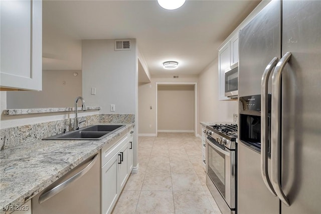 kitchen featuring sink, light tile patterned floors, appliances with stainless steel finishes, light stone countertops, and white cabinets